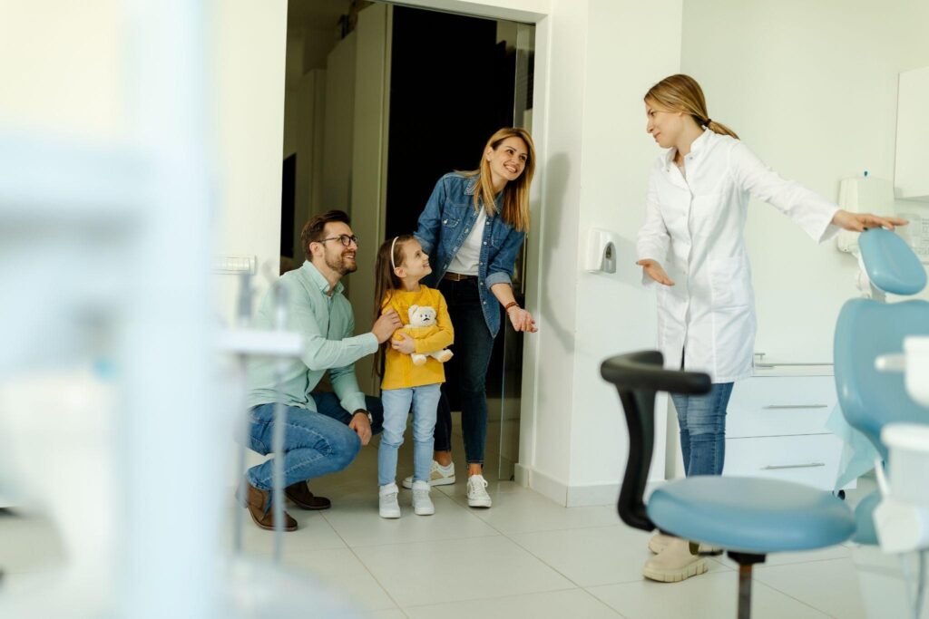 Happy family at a visit to a family health dental clinic. The dentist greets the patients nicely and shows the girl where to sit.