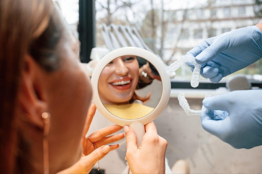 Woman at cosmetic dentistry appointment in Bradenton, Florida, smiling in a mirror while a dentist shows clear aligners; cosmetic dentistry near me for a confident, healthy smile.