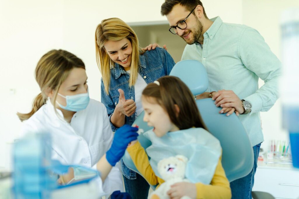 Happy family dental visit – A young girl receives a dental check-up from a female dentist while her smiling parents provide support in a modern Sarasota family dentistry clinic.