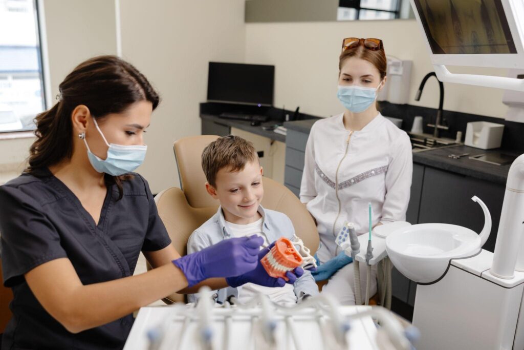Young boy sitting in a dental chair during a pediatric cosmetic dentistry consultation, learning about dental care from a dentist at a family dental clinic.

